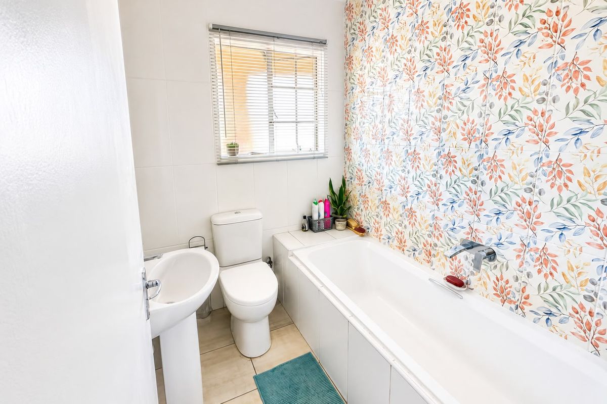 A bright bathroom featuring a pedestal basin, toilet, and a bathtub with a decorative floral tiled feature wall.