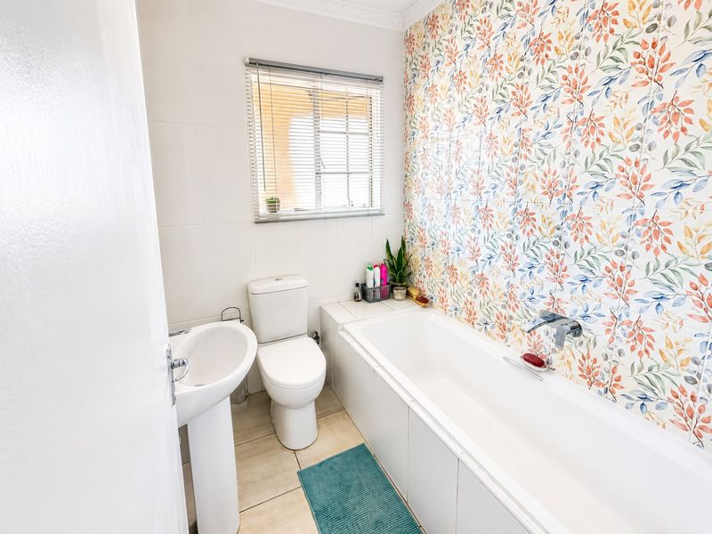 A bright bathroom featuring a pedestal basin, toilet, and a bathtub with a decorative floral tiled feature wall.