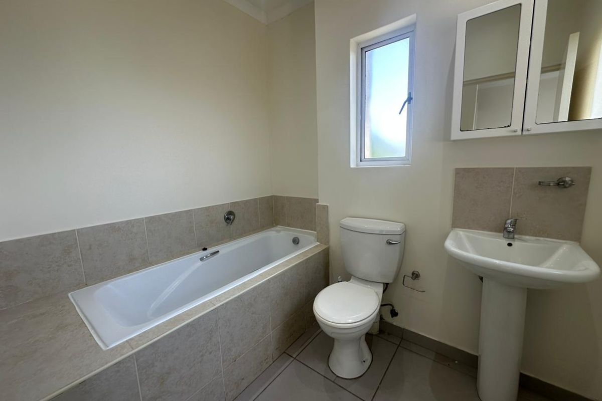 A clean, functional bathroom featuring a built-in bathtub, pedestal basin, toilet, and tiled finishes, offering a neutral and well-maintained space.
