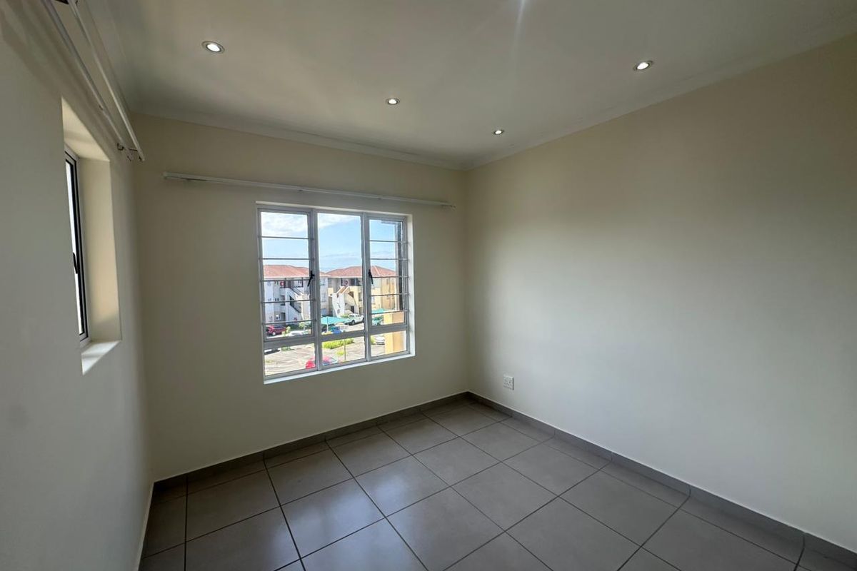 A clean, empty bedroom featuring neutral tiled flooring, recessed downlighting, and large windows with security bars, offering a bright and versatile living space.