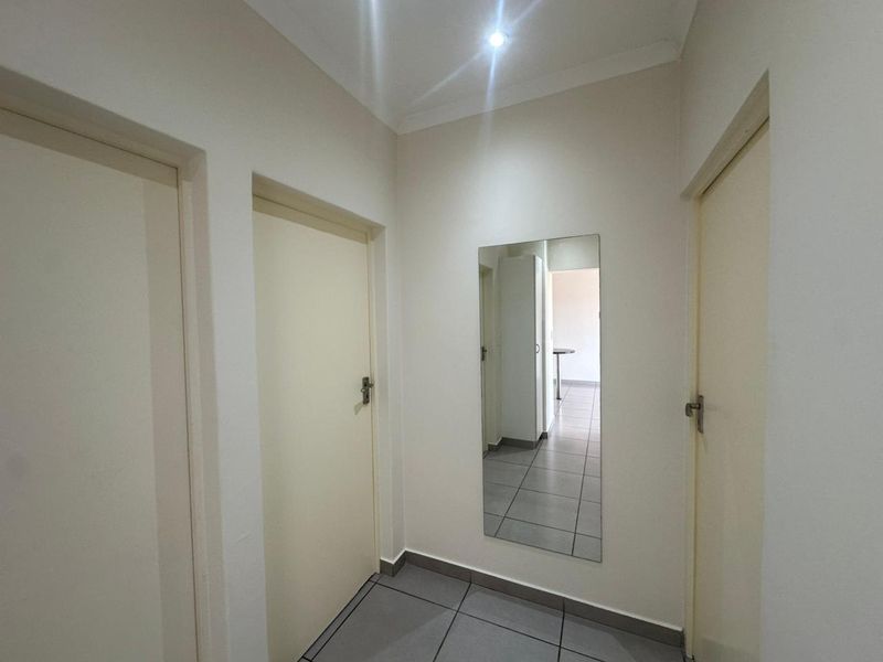A clean and neutral hallway featuring tiled flooring, recessed lighting, and multiple internal doors providing access to adjacent rooms.
