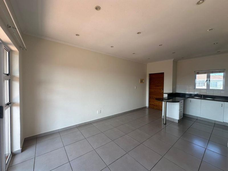 An open-plan living and kitchen area featuring tiled floors, recessed lighting, granite countertops, and a breakfast bar, offering a clean and functional layout.