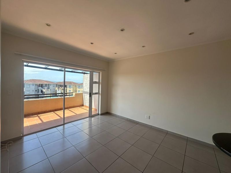 A bright, empty living area featuring neutral tiled flooring, recessed lighting, and large sliding glass doors leading to an outdoor balcony.