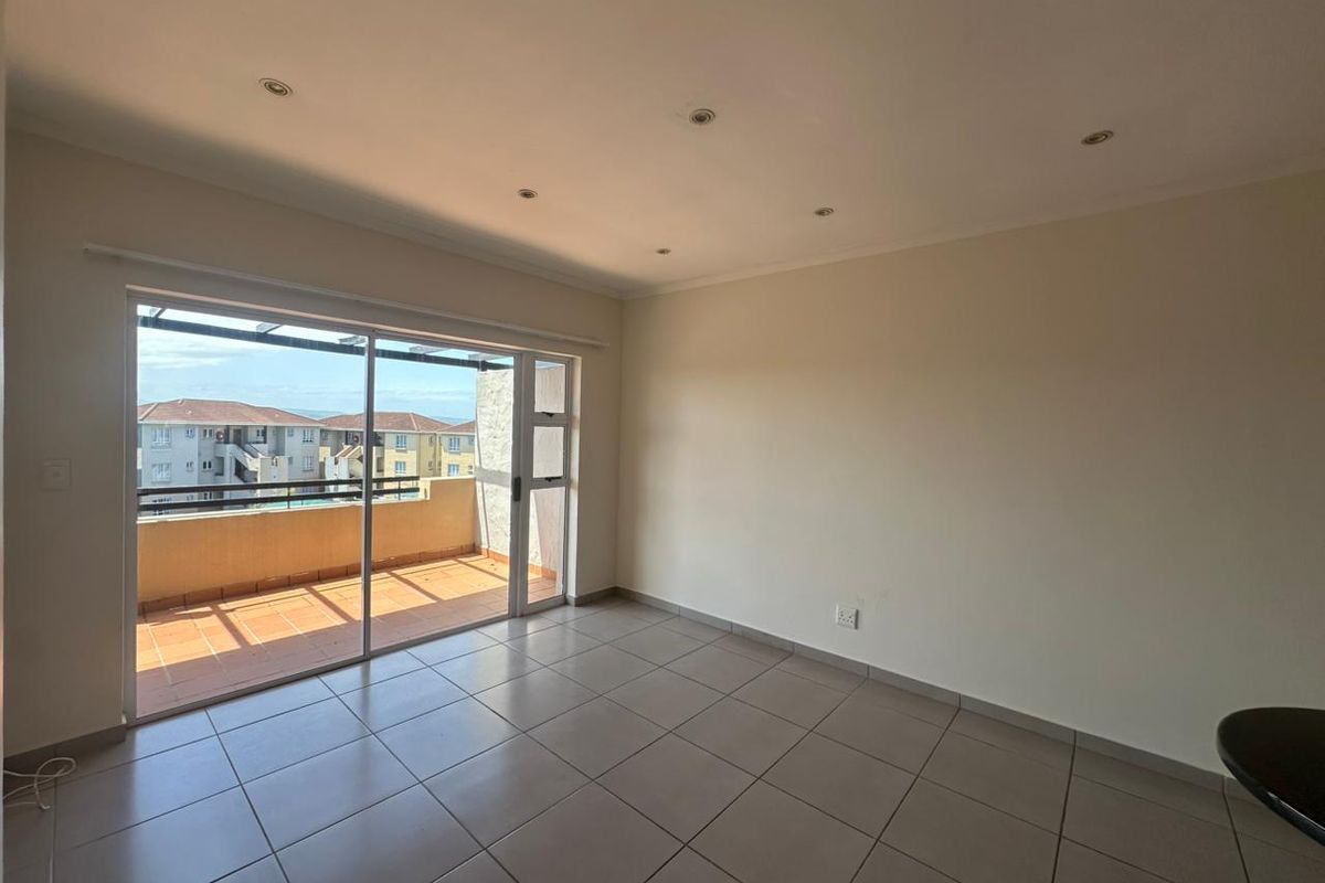 A bright, empty living area featuring neutral tiled flooring, recessed lighting, and large sliding glass doors leading to an outdoor balcony.