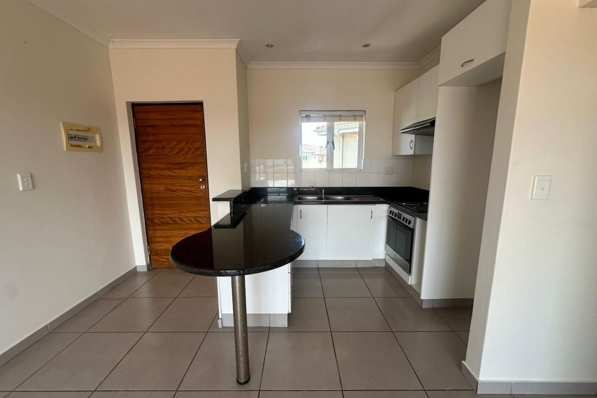 A clean, functional kitchen featuring granite countertops, a breakfast bar, built-in oven, extractor fan, and ample cabinetry with tiled flooring.