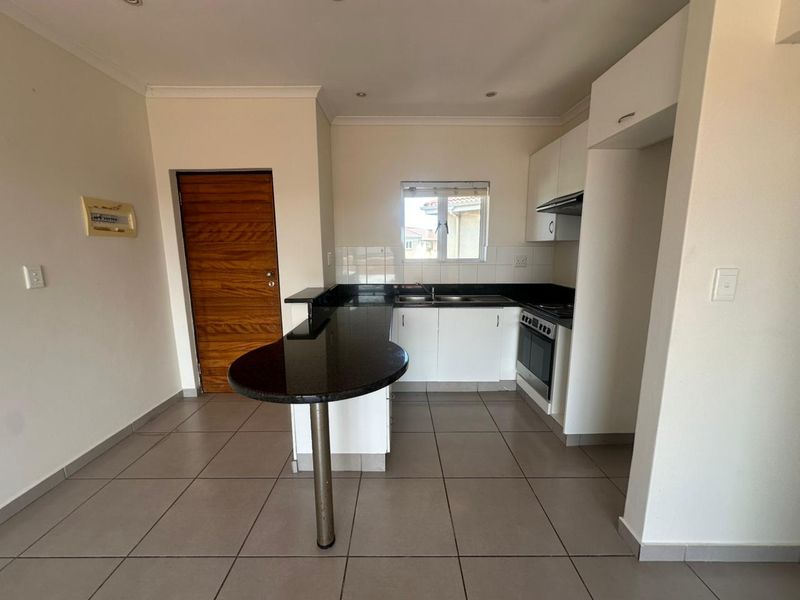 A clean, functional kitchen featuring granite countertops, a breakfast bar, built-in oven, extractor fan, and ample cabinetry with tiled flooring.