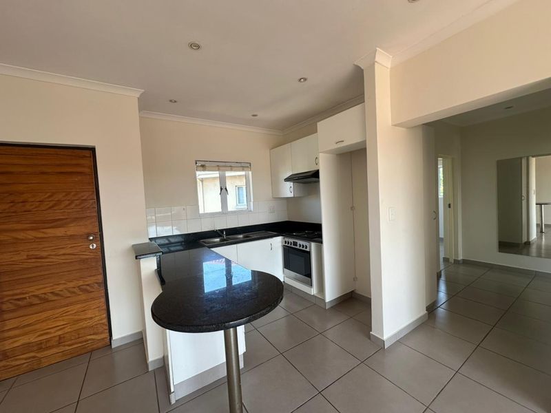A clean, modern kitchen featuring granite countertops, a breakfast bar, built-in oven with extractor fan, and neutral tiled flooring throughout.