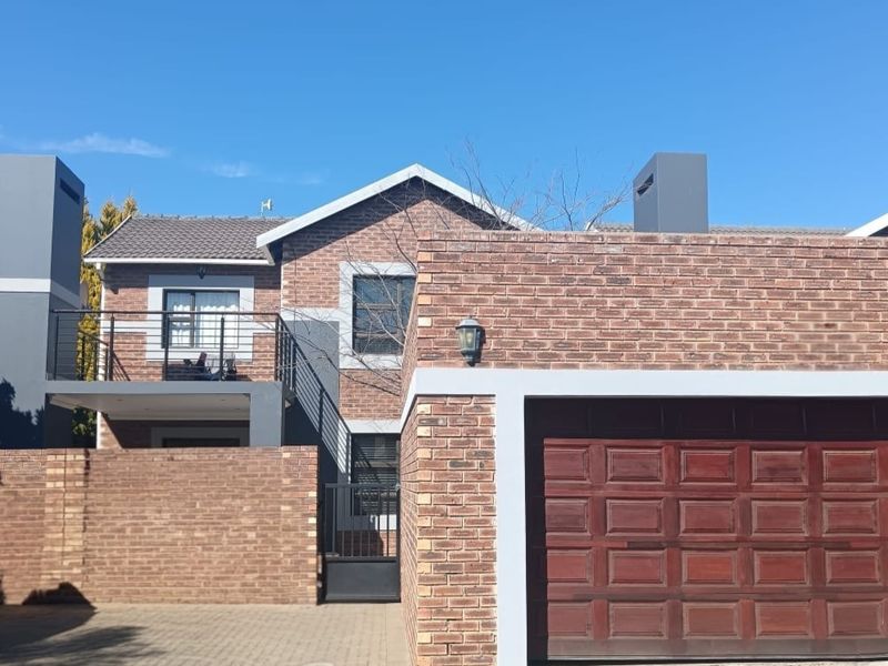 Front elevation of a double-story townhouse featuring a brick facade, paved driveway, and an integrated double garage with a balcony above.