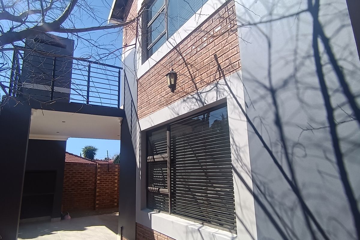 Rear exterior view of the townhouse featuring a brick and rendered facade, a balcony, and a paved patio area with a built-in braai.