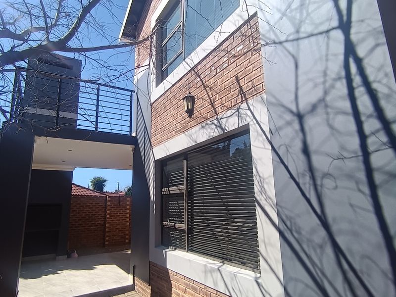 Rear exterior view of the townhouse featuring a brick and rendered facade, a balcony, and a paved patio area with a built-in braai.