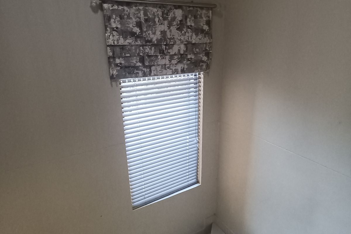 A bright stairwell area featuring a modern stainless steel balustrade, tiled flooring, and a window fitted with venetian blinds.