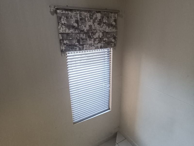 A bright stairwell area featuring a modern stainless steel balustrade, tiled flooring, and a window fitted with venetian blinds.
