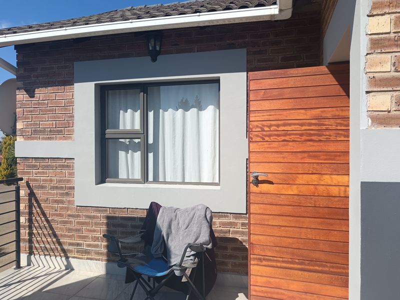 A well-maintained patio area featuring exposed brickwork, a modern timber entrance door, and tiled flooring, providing a clean and functional outdoor transition space.