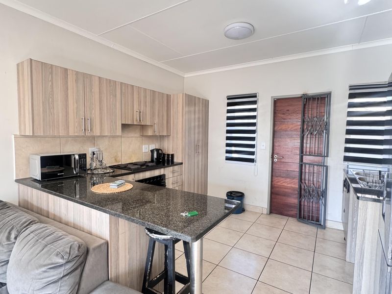 Open-plan kitchen featuring granite countertops, light wood-finish cabinetry, built-in appliances, and ceramic floor tiles, with direct access to an exterior security door.