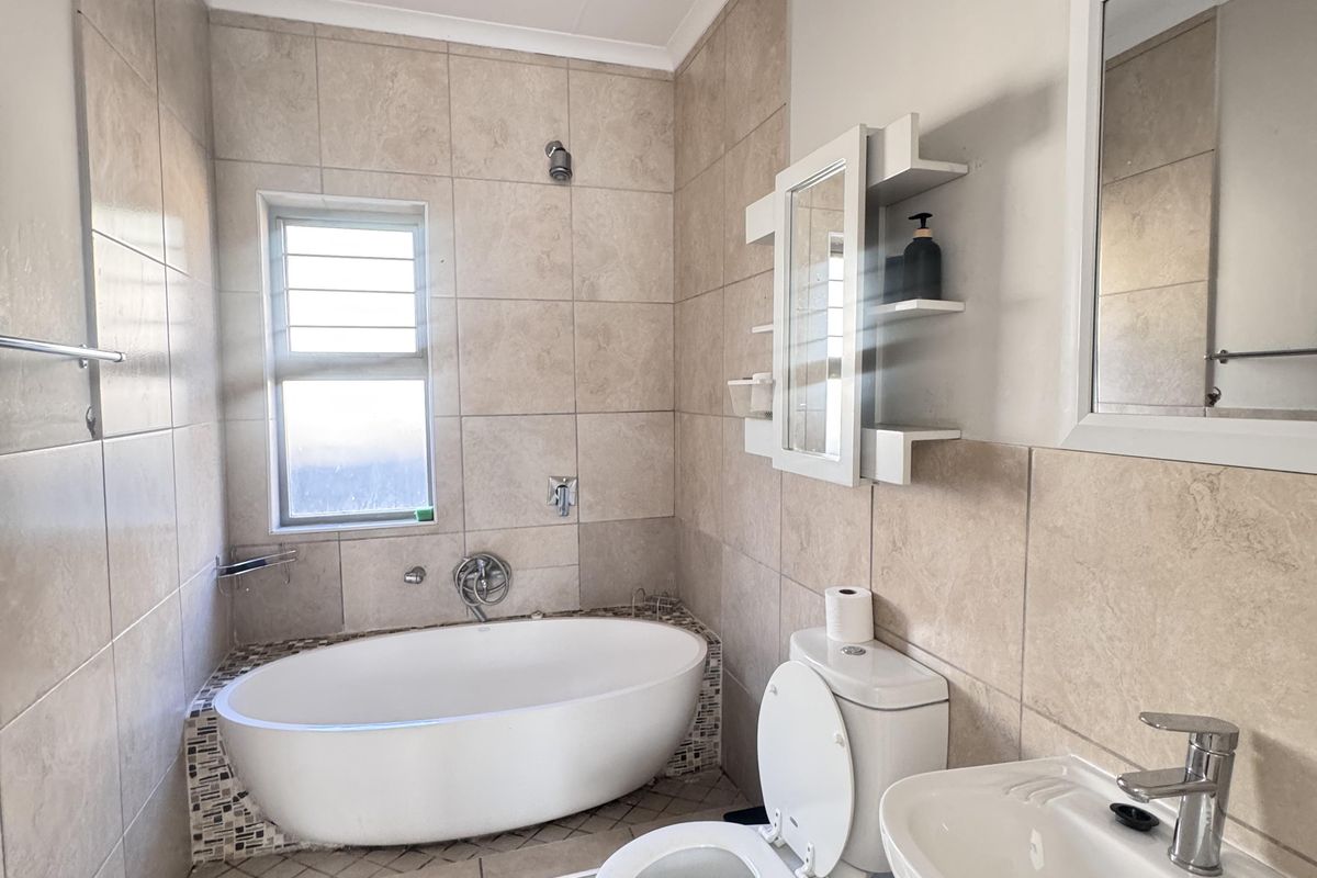 A functional bathroom featuring a freestanding bathtub, pedestal basin, toilet, and neutral wall tiling with built-in shelving.