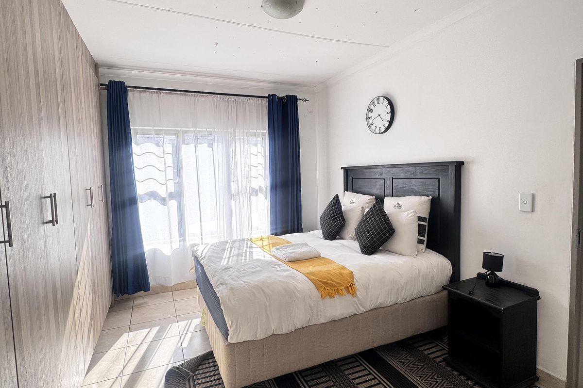 A well-lit bedroom featuring built-in cupboards, tiled flooring, and large windows allowing for natural light.