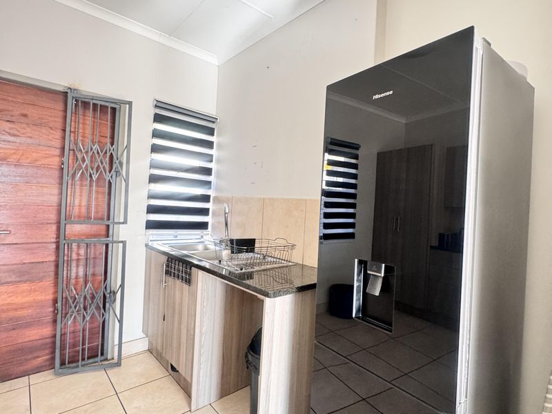 Compact scullery area featuring granite countertops, stainless steel sink, tiled flooring, and direct access to the exterior via a security gate.