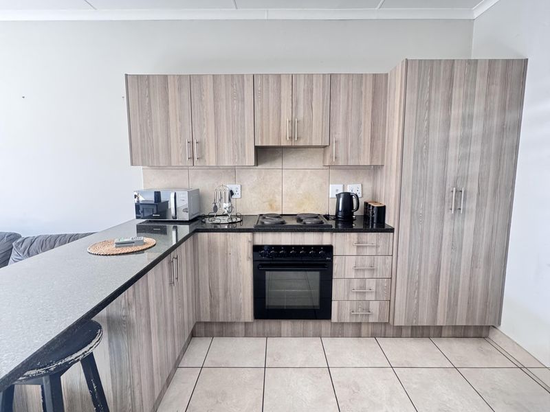 A functional kitchen featuring wood-look cabinetry, dark laminate countertops, a built-in oven and hob, and tiled flooring with an integrated breakfast bar.