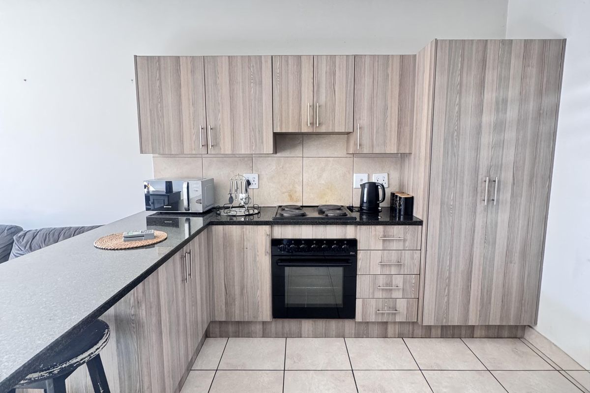 A functional kitchen featuring wood-look cabinetry, dark laminate countertops, a built-in oven and hob, and tiled flooring with an integrated breakfast bar.