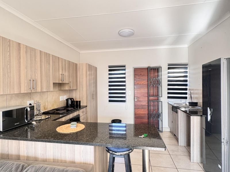 Modern open-plan kitchen featuring granite countertops, light wood-finish cabinetry, built-in appliances, and tiled flooring, seamlessly integrated with the living area.