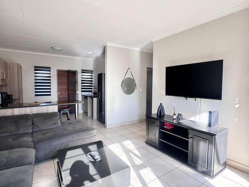 Open-plan living area featuring tiled flooring, a modern kitchen with island, and direct access to the exterior via a security gate.