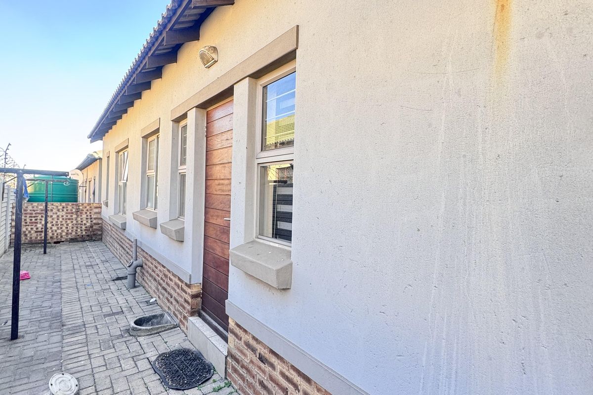 Rear exterior view of the townhouse featuring a paved walkway, brick base detailing, and a timber entrance door.