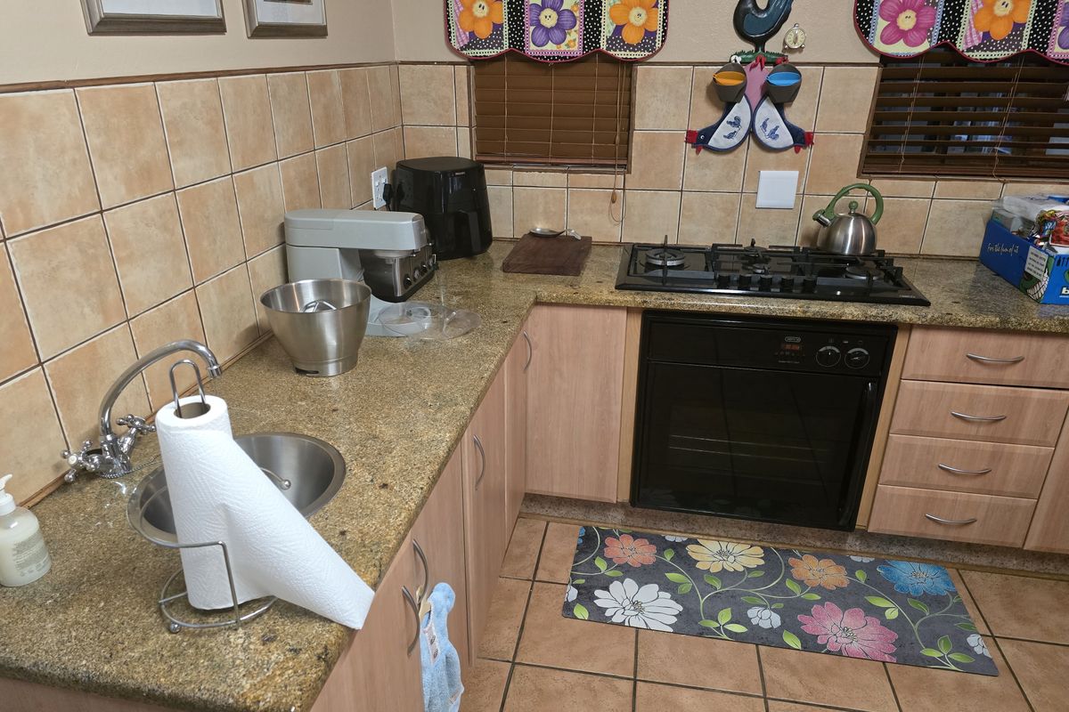A functional kitchen featuring granite countertops, light wood-finish cabinetry, a built-in oven with gas hob, and ceramic tile flooring and backsplash.