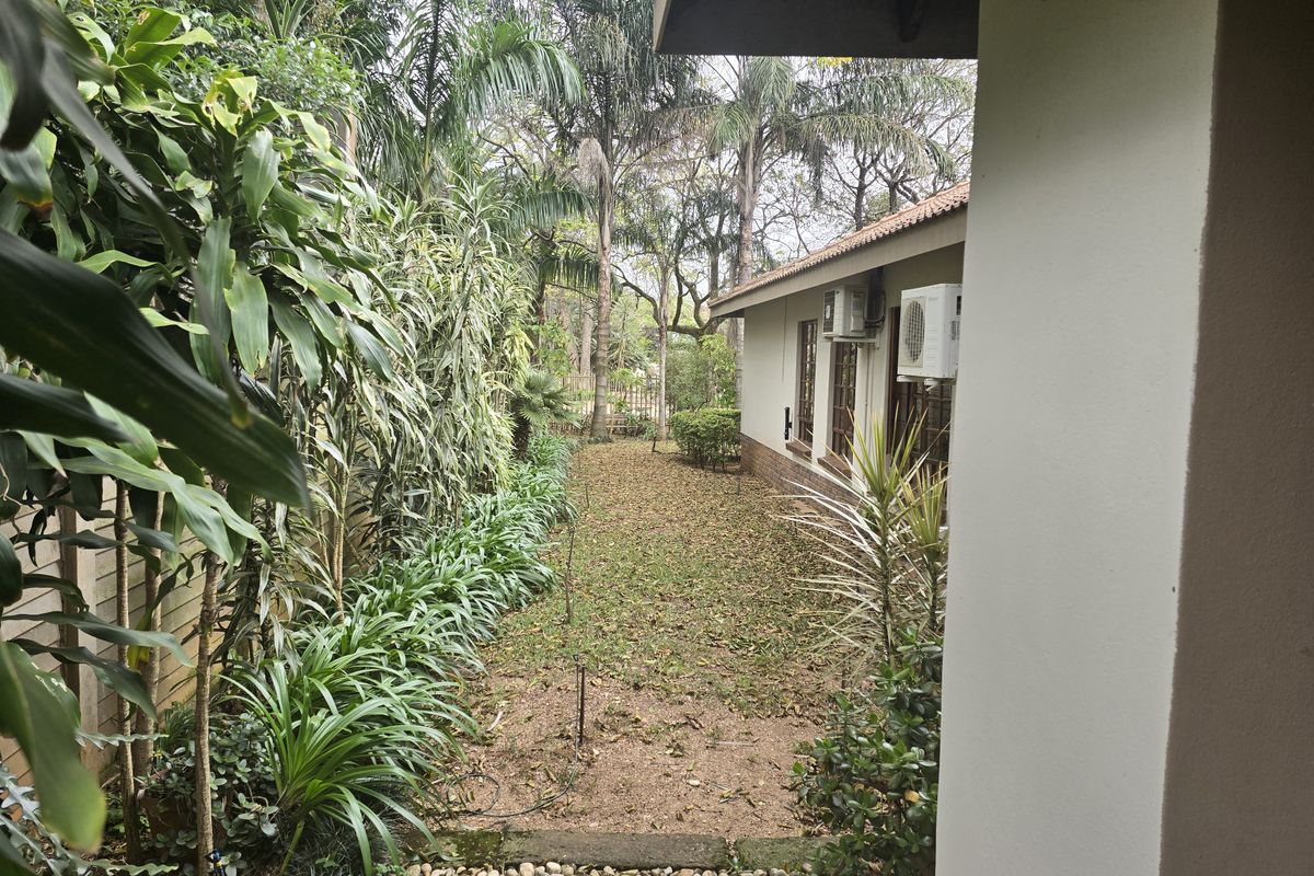 A view of the rear garden area featuring established landscaping, a pebble path, and exterior wall-mounted air conditioning units.