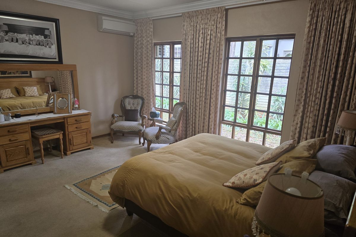 Spacious bedroom featuring carpet flooring, crown molding, a wall-mounted air conditioning unit, and large french doors providing natural light and garden access.
