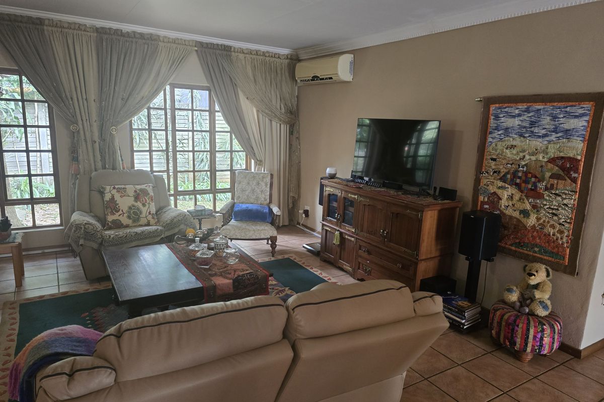 A comfortable living room featuring tiled flooring, a wall-mounted air conditioning unit, and large glass sliding doors providing natural light and garden access.