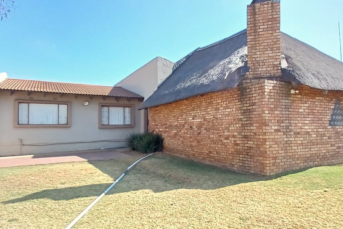 Rear view of the property featuring a combination of thatch and tiled roofing, exposed brickwork, and a paved patio area overlooking the garden.