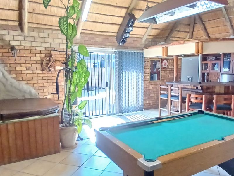 Spacious entertainment area featuring a built-in bar, thatched roof, exposed brickwork, and tiled flooring, ideal for hosting guests.
