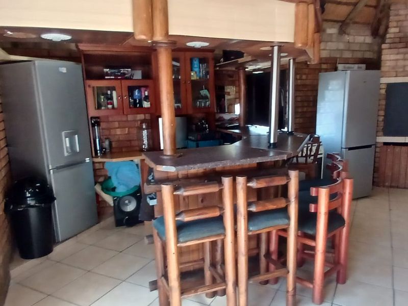 Rustic indoor entertainment area featuring a built-in bar counter, brick fireplace, and tiled flooring, offering a cozy space for social gatherings.