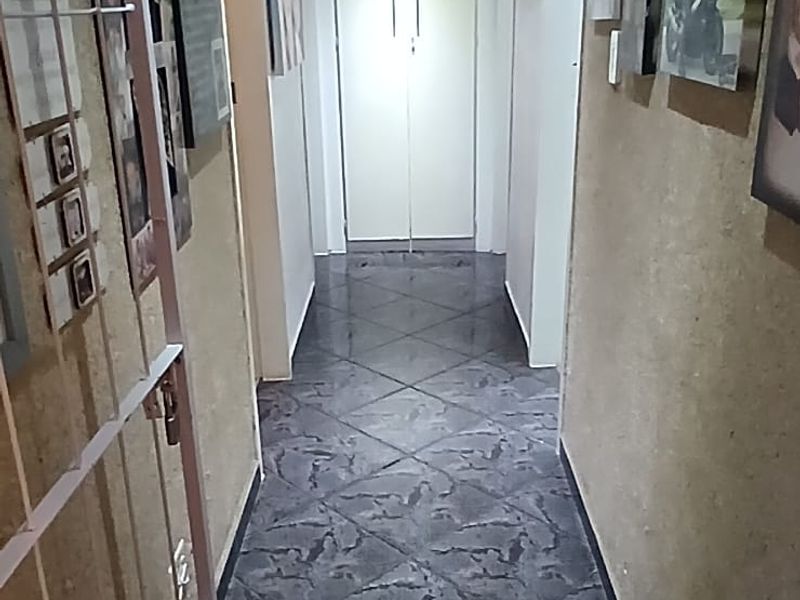 A well-lit hallway featuring dark patterned floor tiles and a built-in storage cupboard at the end of the corridor.