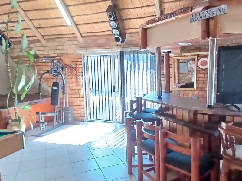 A rustic entertainment area featuring a built-in bar, exposed brick walls, and a traditional thatched roof, offering a casual space for social gatherings.