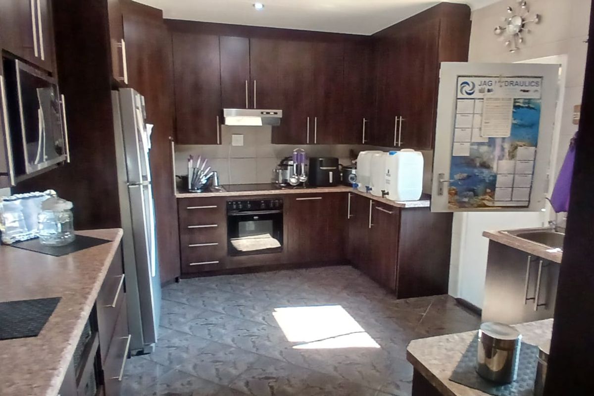 A functional kitchen featuring dark wood cabinetry, laminate countertops, built-in oven, electric hob, and tiled flooring.