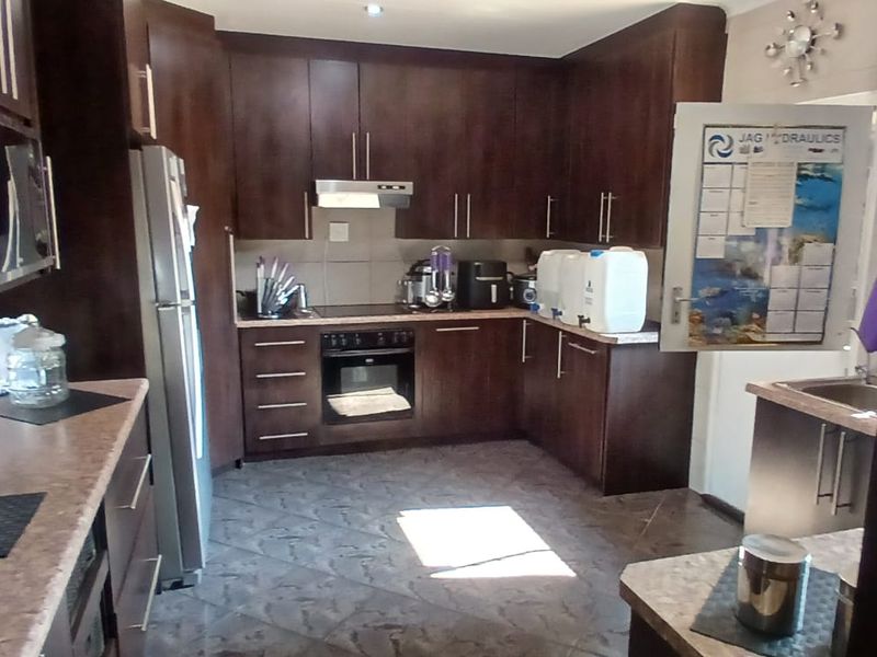 A functional kitchen featuring dark wood cabinetry, laminate countertops, built-in oven, electric hob, and tiled flooring.