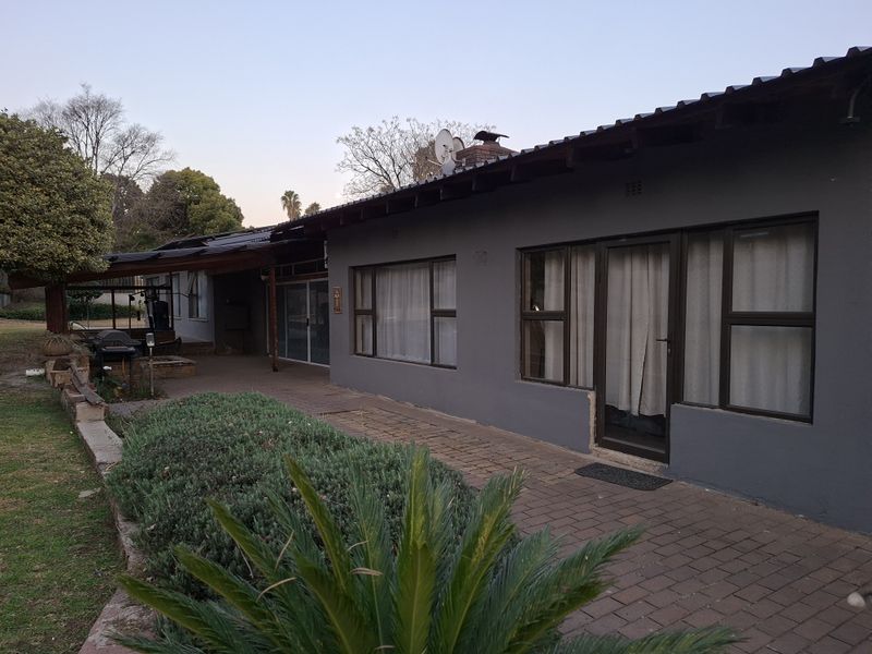 Rear exterior view of the house featuring a paved patio area, dark grey painted walls, and aluminium window frames.