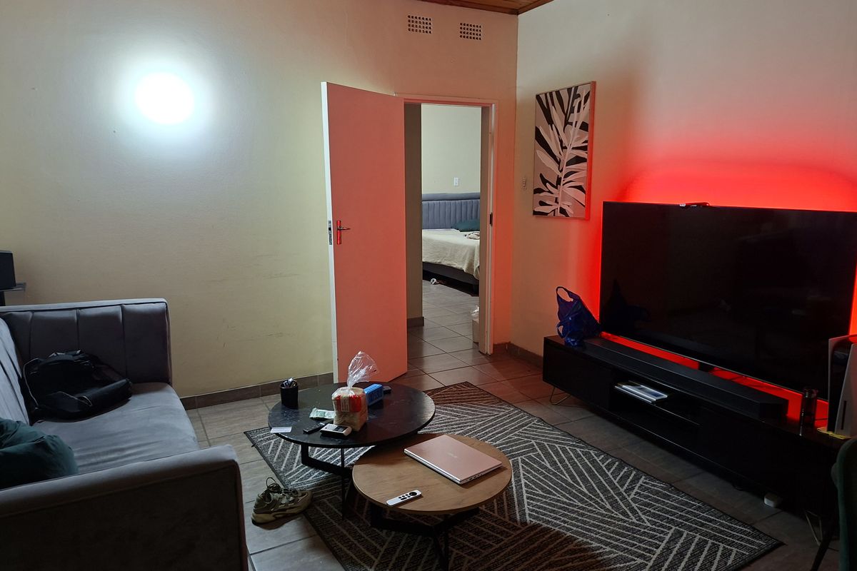 A living room featuring tiled flooring and a timber ceiling, with an open doorway leading to an adjacent bedroom.