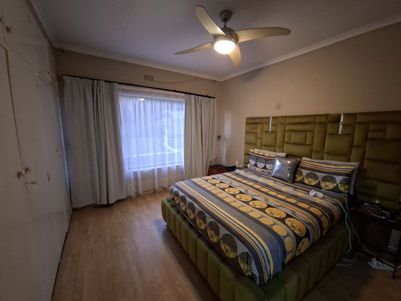 A bedroom featuring laminate flooring, built-in cupboards, and a ceiling fan, providing a functional and comfortable sleeping space.
