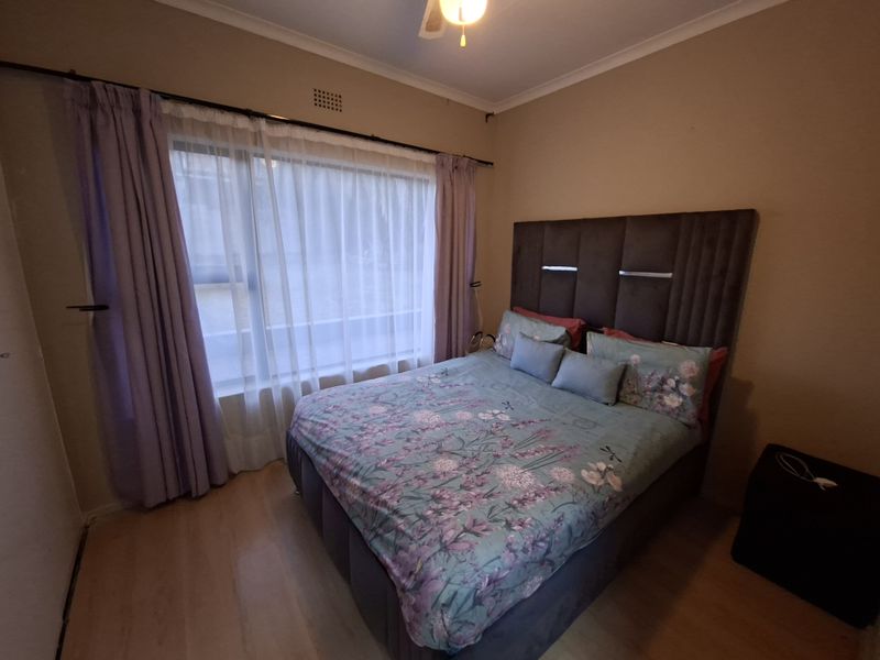 A standard bedroom featuring laminate flooring, a ceiling fan, and a large window with curtain fixtures.