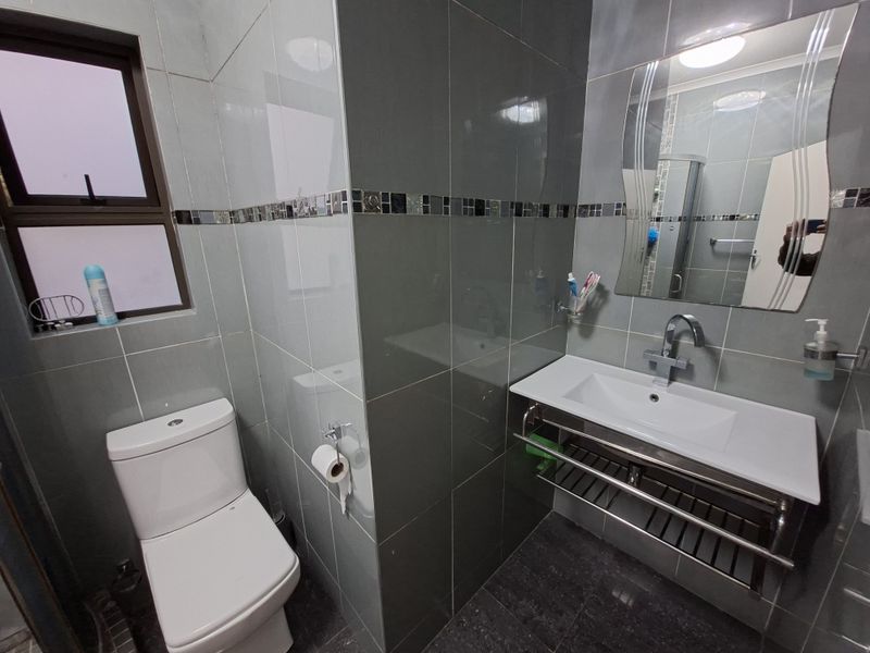 Modern bathroom featuring grey wall tiles, a wall-mounted vanity basin with chrome fixtures, and a standard toilet.