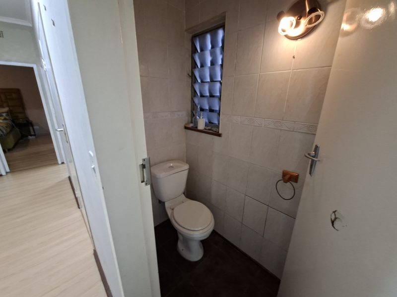 A compact guest bathroom featuring tiled walls, a standard toilet, and a louver window, currently requiring minor repairs to the door hardware.