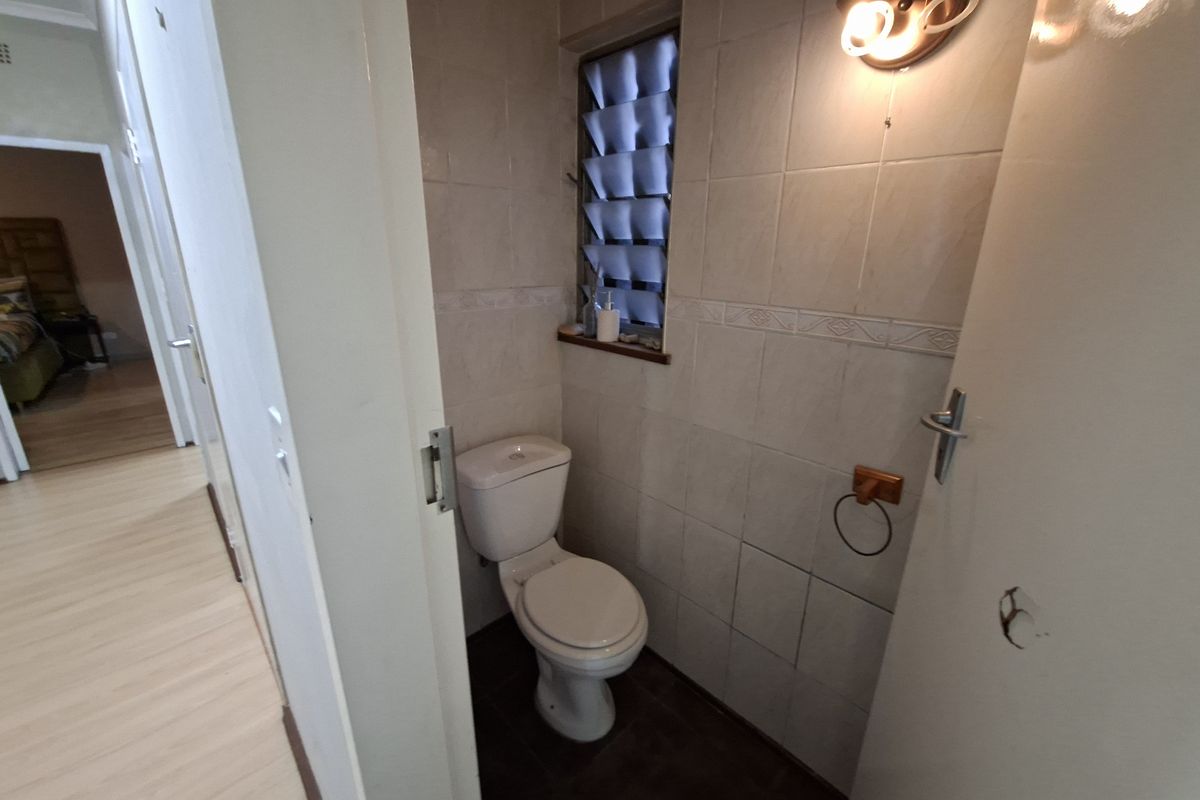 A compact guest bathroom featuring tiled walls, a standard toilet, and a louver window, currently requiring minor repairs to the door hardware.