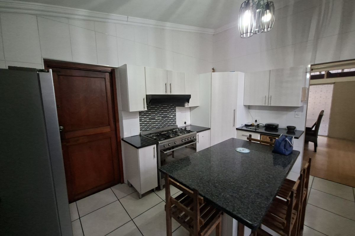 A functional kitchen featuring white cabinetry, granite countertops, a central island, and a gas stove with an extractor fan.