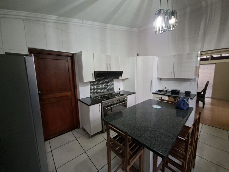 A functional kitchen featuring white cabinetry, granite countertops, a central island, and a gas stove with an extractor fan.