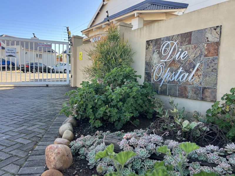 Entrance view of the Die Opstal complex featuring a secure gated access point, paved driveway, and landscaped boundary wall.