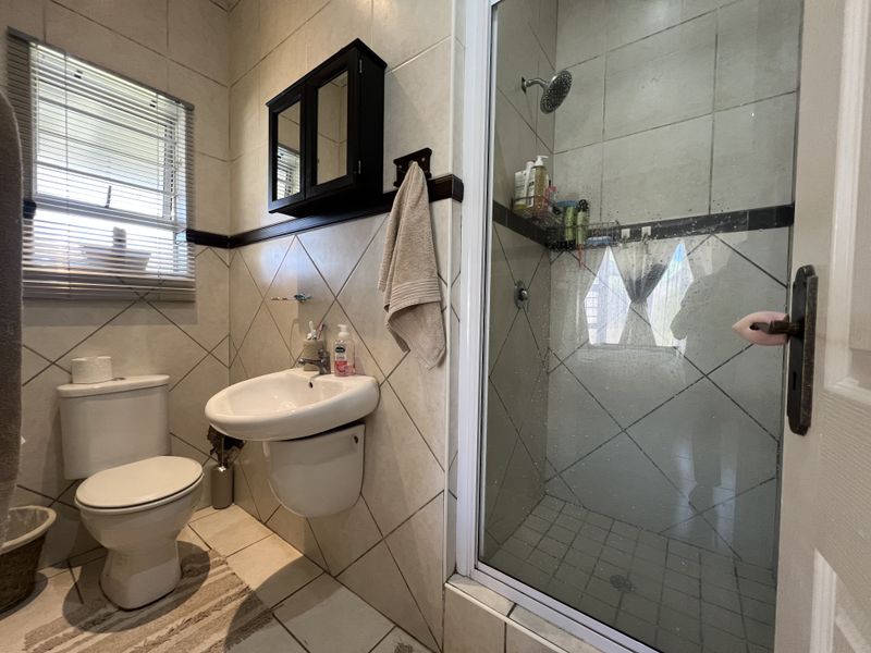 A functional bathroom featuring a wall-mounted basin, toilet, and a glass-enclosed shower with tiled finishes throughout.