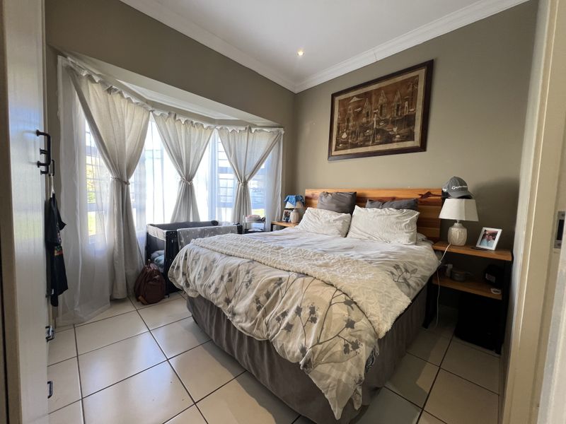 A well-maintained bedroom featuring tiled flooring, a large bay window allowing natural light, and classic cornice detailing.