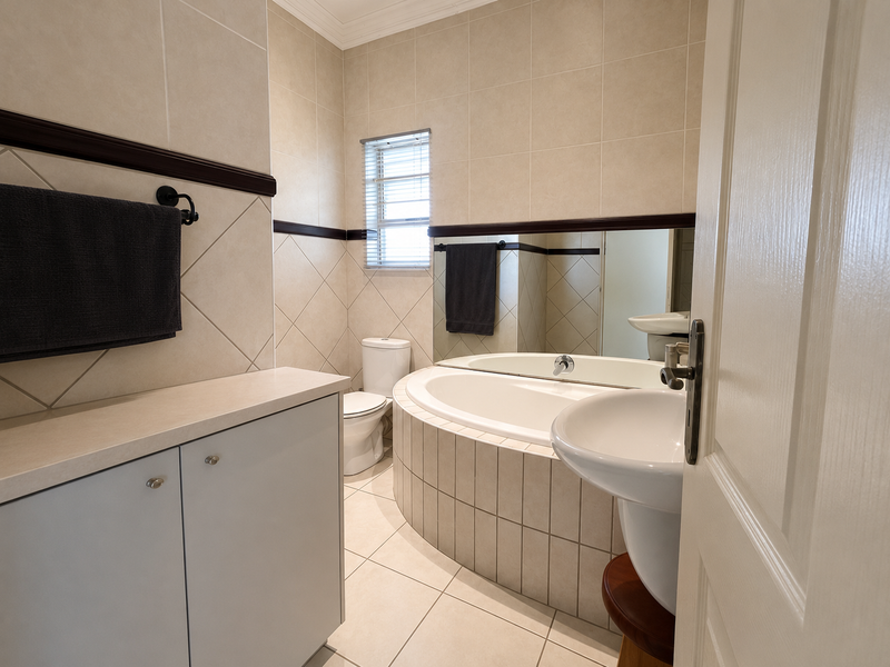A well-maintained bathroom featuring a tiled bathtub surround, pedestal washbasin, built-in vanity storage, and neutral wall tiling.